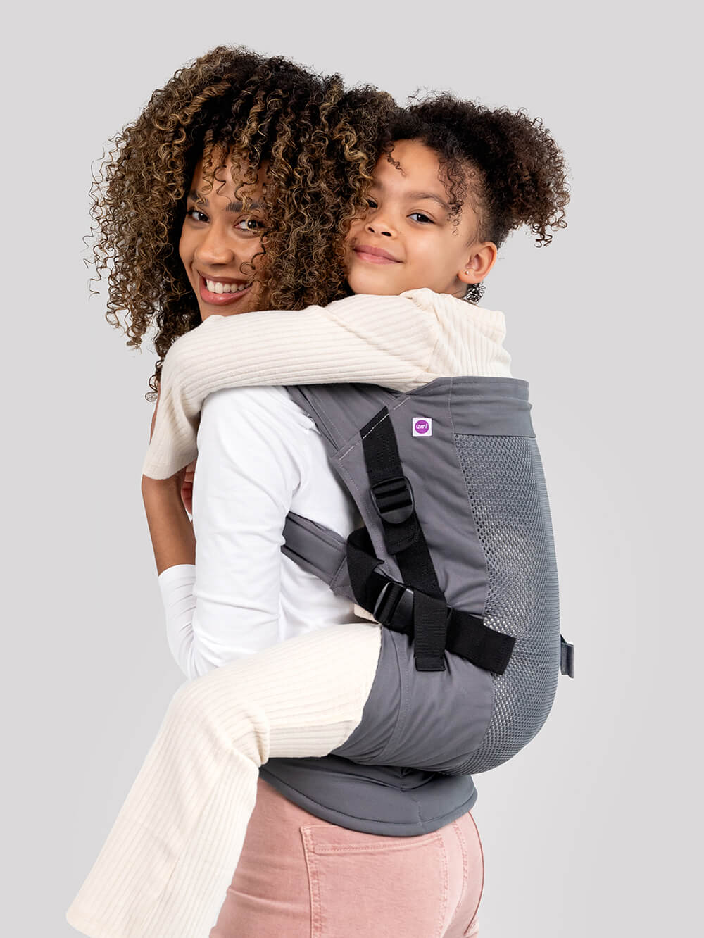 Woman carrying a child in Izmi Adventure Carrier in ghosted grey.